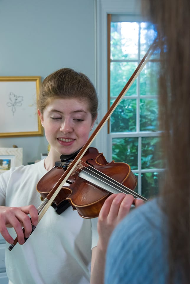 A happy young student playing the violin for her teacher