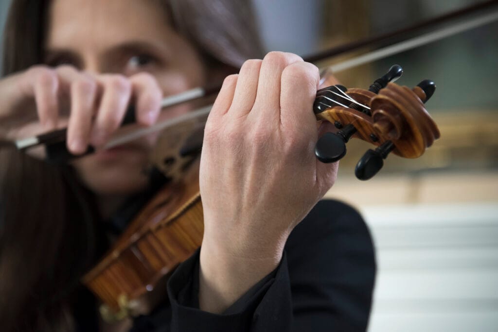 dramatic photo of Christine playing her violin. Her left hand and the neck of the violin in focus.