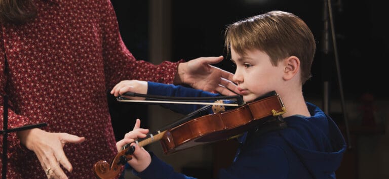 young violin student in a lesson. Instructor corrects posture and technique